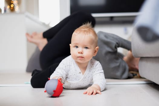 Happy family moments. Mother lying comfortably on children's mat watching and suppervising her baby boy playinghis in living room. Positive human emotions, feelings, joy.