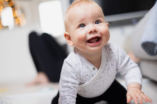 Cute infant baby boy playing, crawling and standing up by living room sofa at home. Baby playing at home