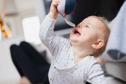 Cute infant baby boy playing, crawling and standing up by living room sofa at home. Baby playing at home