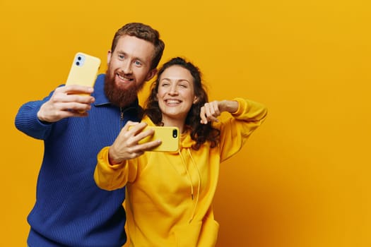 Man and woman couple smiling merrily with phone in hand social media viewing photos and videos, on yellow background, symbols signs and hand gestures, family freelancers. High quality photo