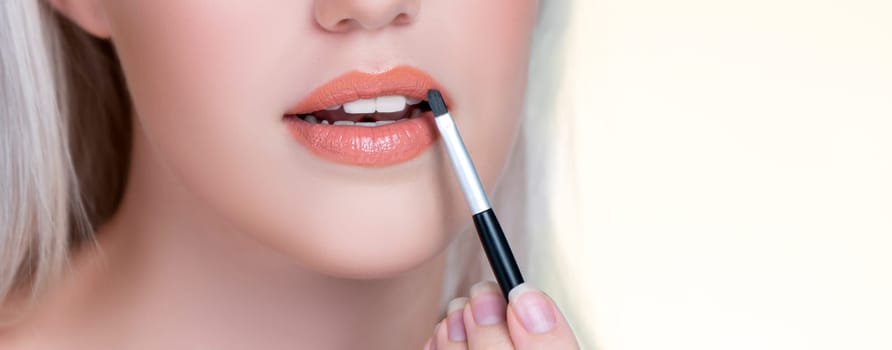 Closeup personable young woman with flawless healthy skin and natural makeup putting fashion glossy lipstick on her lip with lip brush in isolated background. Facial cosmetic makeup in process.
