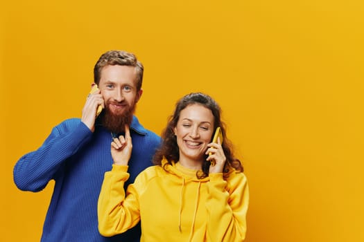 Man and woman couple smiling merrily with phone in hand social media viewing photos and videos, on yellow background, symbols signs and hand gestures, family freelancers. High quality photo