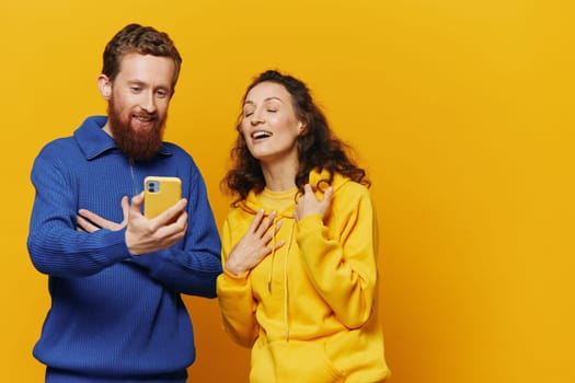 Man and woman couple smiling merrily with phone in hand social media viewing photos and videos, on yellow background, symbols signs and hand gestures, family freelancers. High quality photo