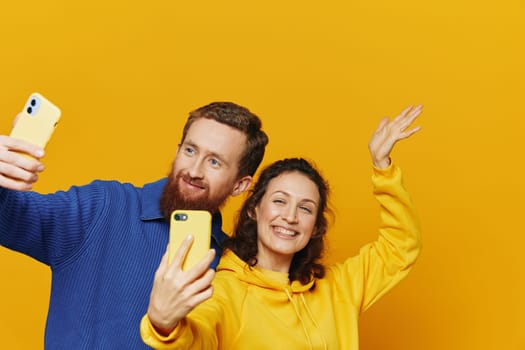 Man and woman couple smiling merrily with phone in hand social media viewing photos and videos, on yellow background, symbols signs and hand gestures, family freelancers. High quality photo