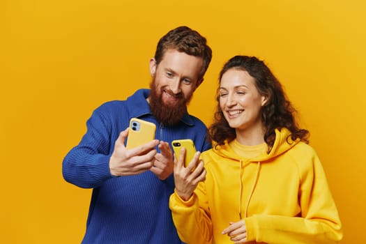 Man and woman couple smiling merrily with phone in hand social media viewing photos and videos, on yellow background, symbols signs and hand gestures, family freelancers. High quality photo