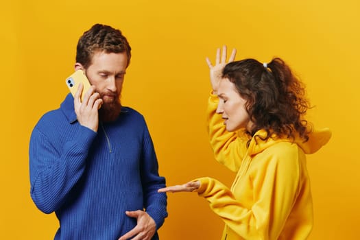 Man and woman couple with phone in hand call talking on the phone, on a yellow background, symbols signs and hand gestures, family quarrel jealousy and scandal. High quality photo