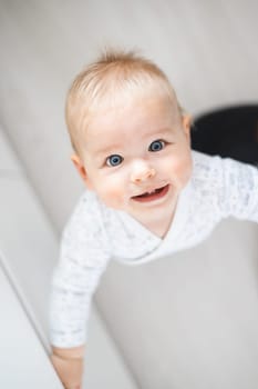 top down view of cheerful baby boy infant taking first steps holding to kitchen drawer at home. Cute baby boy learning to walk.