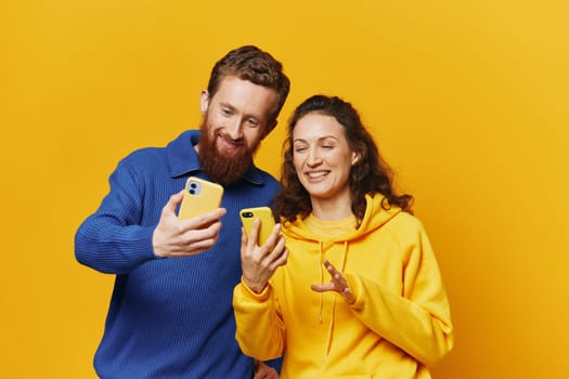 Man and woman couple smiling merrily with phone in hand social media viewing photos and videos, on yellow background, symbols signs and hand gestures, family freelancers. High quality photo