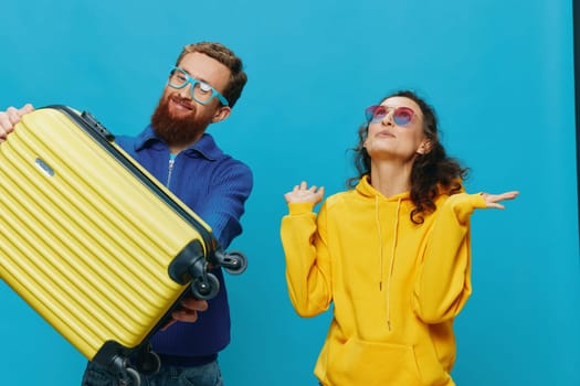 Woman and man smile sitting on suitcase with yellow suitcase smile, on blue background, packing for trip, family vacation trip. High quality photo