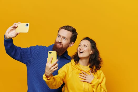 Man and woman couple smiling merrily with phone in hand social media viewing photos and videos, on yellow background, symbols signs and hand gestures, family freelancers. High quality photo