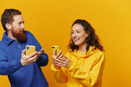 Man and woman couple smiling merrily with phone in hand social media viewing photos and videos, on yellow background, symbols signs and hand gestures, family freelancers. High quality photo