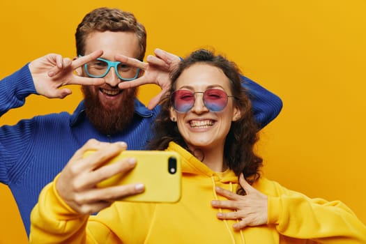 Woman and man funny couple with phones in hand social networking and communication crooked do selfies smile fun, on yellow background. The concept of real family relationships, freelancers, work online. High quality photo