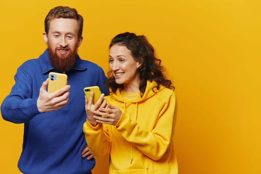 Man and woman couple smiling merrily with phone in hand social media viewing photos and videos, on yellow background, symbols signs and hand gestures, family freelancers. High quality photo