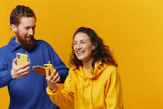 Man and woman couple smiling merrily with phone in hand social media viewing photos and videos, on yellow background, symbols signs and hand gestures, family freelancers. High quality photo