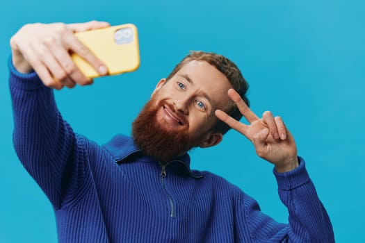 Portrait of a man with a phone in his hands blogger takes selfies, on a blue background. Communicating online social media, lifestyle. High quality photo