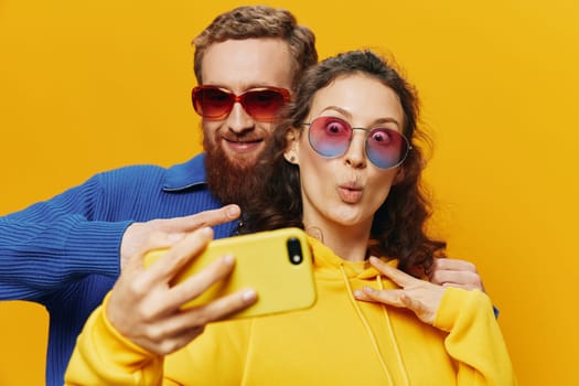 Woman and man funny couple with phones in hand social networking and communication crooked do selfies smile fun, on yellow background. The concept of real family relationships, freelancers, work online. High quality photo