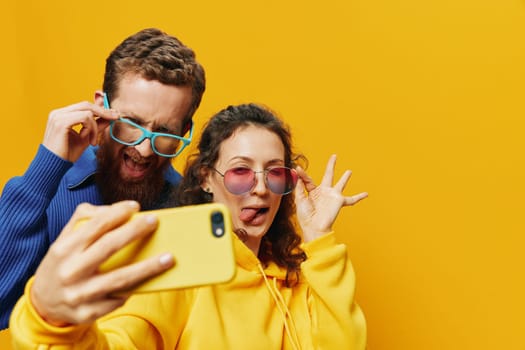 Woman and man funny couple with phones in hand social networking and communication crooked do selfies smile fun, on yellow background. The concept of real family relationships, freelancers, work online. High quality photo