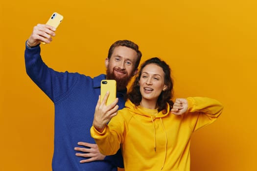 Man and woman couple smiling merrily with phone in hand social media viewing photos and videos, on yellow background, symbols signs and hand gestures, family freelancers. High quality photo