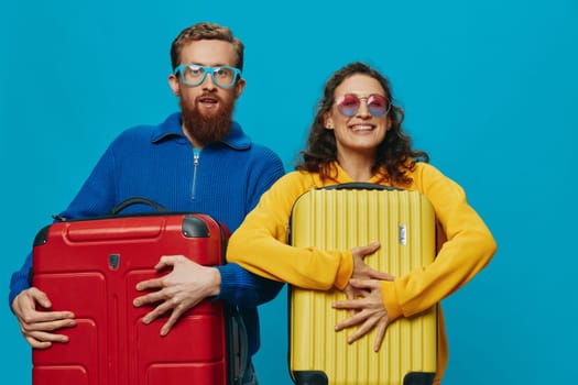 Woman and man smile suitcases in hand with yellow and red suitcase smile fun, on blue background, packing for a trip, family vacation trip. High quality photo