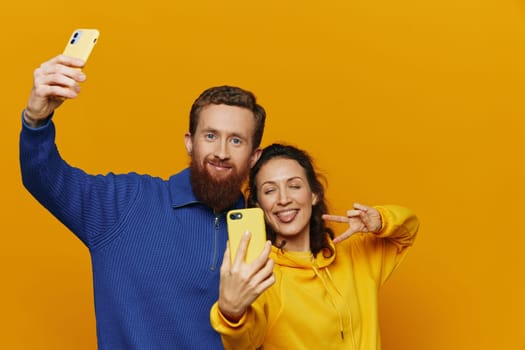 Man and woman couple smiling merrily with phone in hand social media viewing photos and videos, on yellow background, symbols signs and hand gestures, family freelancers. High quality photo