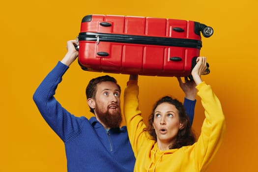 Woman and man smiling, suitcases in hand with yellow and red suitcase smiling merrily and crooked, yellow background, going on a trip, family vacation trip, newlyweds. High quality photo