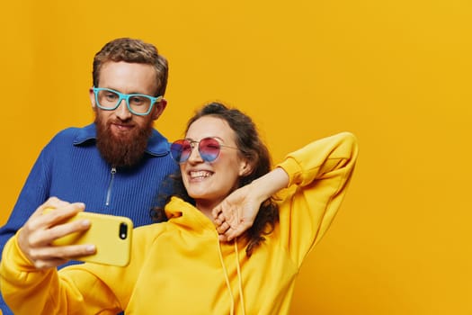 Woman and man funny couple with phones in hand social networking and communication crooked do selfies smile fun, on yellow background. The concept of real family relationships, freelancers, work online. High quality photo