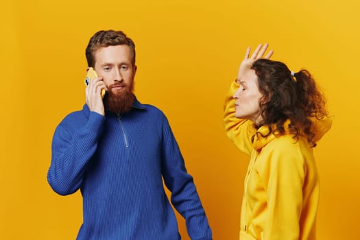 Man and woman couple with phone in hand call talking on the phone, on a yellow background, symbols signs and hand gestures, family quarrel jealousy and scandal. High quality photo