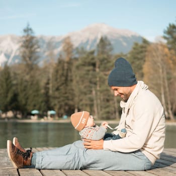 Happy family. Father playing with her baby boy infant oudoors on sunny autumn day. Portrait of dad and little son on wooden platform by lake. Positive human emotions, feelings, joy