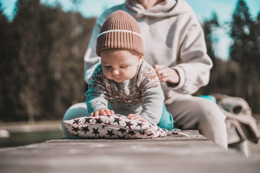 Happy family. Young mother playing with her baby boy infant oudoors on sunny autumn day. Portrait of mom and little son on wooden platform by lake. Positive human emotions, feelings, joy