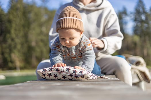 Happy family. Young mother playing with her baby boy infant oudoors on sunny autumn day. Portrait of mom and little son on wooden platform by lake. Positive human emotions, feelings, joy