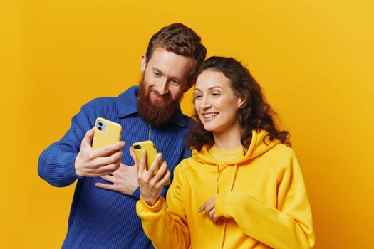 Man and woman couple smiling merrily with phone in hand social media viewing photos and videos, on yellow background, symbols signs and hand gestures, family freelancers. High quality photo