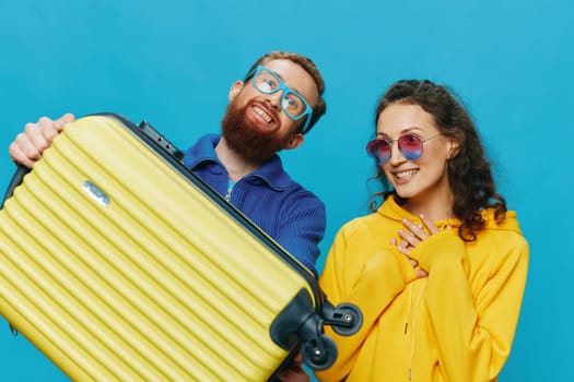 Woman and man smile sitting on suitcase with yellow suitcase smile, on blue background, packing for trip, family vacation trip. High quality photo