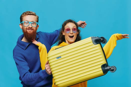 Woman and man smile sitting on suitcase with yellow suitcase smile, on blue background, packing for trip, family vacation trip. High quality photo