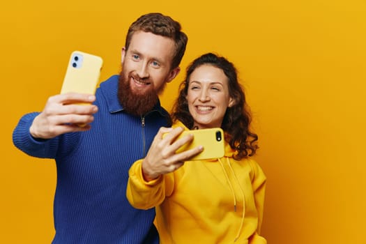 Man and woman couple smiling merrily with phone in hand social media viewing photos and videos, on yellow background, symbols signs and hand gestures, family freelancers. High quality photo