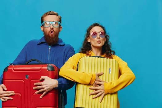 Woman and man smile suitcases in hand with yellow and red suitcase smile fun, on blue background, packing for a trip, family vacation trip. High quality photo