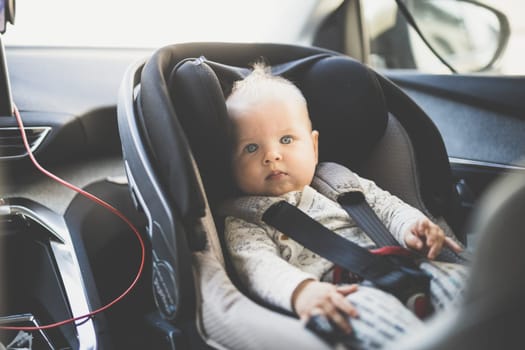 Cute little baby boy strapped into infant car seat in passenger compartment during car drive
