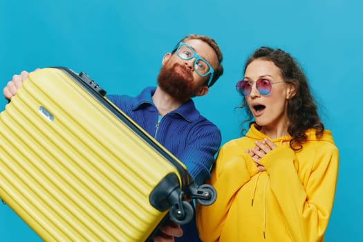 Woman and man smile sitting on suitcase with yellow suitcase smile, on blue background, packing for trip, family vacation trip. High quality photo