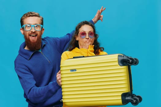 Woman and man smile sitting on suitcase with yellow suitcase smile, on blue background, packing for trip, family vacation trip. High quality photo