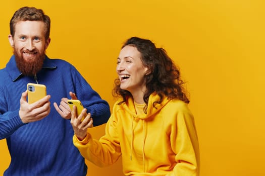 Man and woman couple smiling merrily with phone in hand social media viewing photos and videos, on yellow background, symbols signs and hand gestures, family freelancers. High quality photo