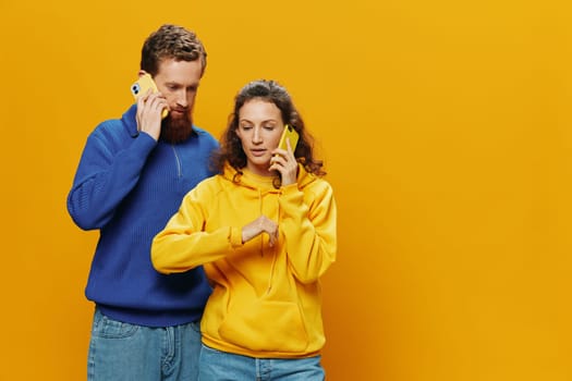 Man and woman couple smiling merrily with phone in hand social media viewing photos and videos, on yellow background, symbols signs and hand gestures, family freelancers. High quality photo