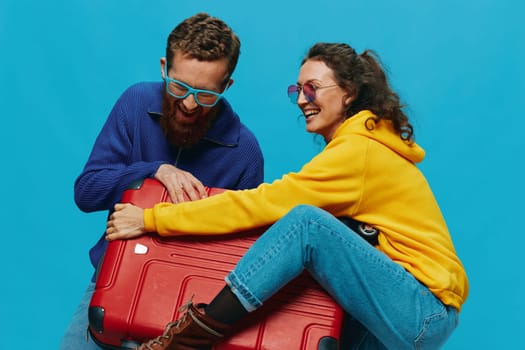 Woman and man smile suitcases in hand with yellow and red suitcase smile fun, on blue background, packing for a trip, family vacation trip. High quality photo