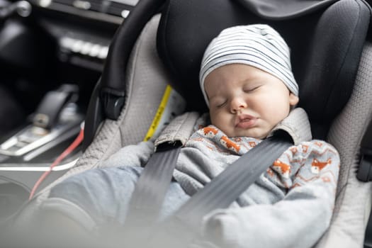 Cute little baby boy sleeping strapped into infant car seat in passenger compartment during car drive