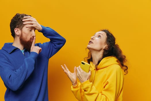 Woman and man cheerful couple with phones in hand social networking and communication crooked smile fun and fight, in yellow background. The concept of real family relationships, freelancers, work online. High quality photo