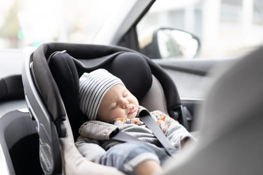 Cute little baby boy sleeping strapped into infant car seat in passenger compartment during car drive