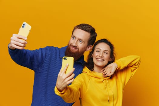 Man and woman couple smiling merrily with phone in hand social media viewing photos and videos, on yellow background, symbols signs and hand gestures, family freelancers. High quality photo