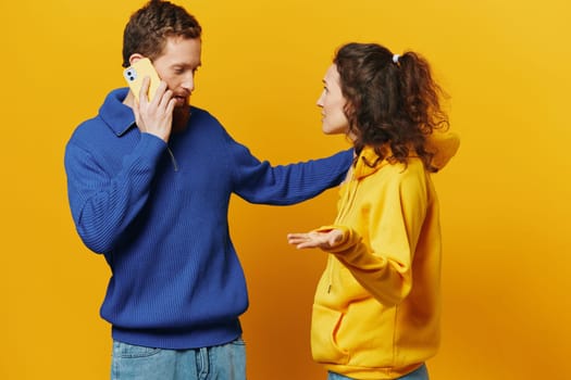 Man and woman couple with phone in hand call talking on the phone, on a yellow background, symbols signs and hand gestures, family quarrel jealousy and scandal. High quality photo