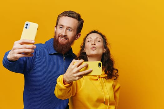 Man and woman couple smiling merrily with phone in hand social media viewing photos and videos, on yellow background, symbols signs and hand gestures, family freelancers. High quality photo