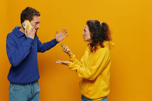 Woman and man cheerful couple with phones in hand social networking and communication crooked smile fun and fight, in yellow background. The concept of real family relationships, freelancers, work online. High quality photo