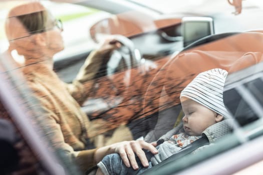 Mother concentrating on driving family car running errands while her baby sleeps in infant car seat by her site