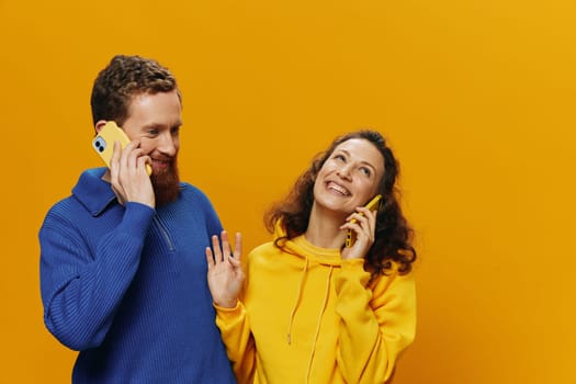 Woman and man cheerful couple with phones in hand talking on cell phone crooked smile cheerful, on yellow background. The concept of real family relationships, talking on the phone, work online. High quality photo